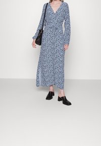 Šaty s dlouhými rukávy a zavinovacím stylem ve světle modré barvě s květinovým vzorem. Doplněné o černé muly na blokovém podpatku a malou černou kabelku.
