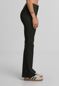 Černé pruhované zvonové kalhoty s vysokým pasem a texturovanou tkaninou, v kombinaci s béžovými teniskami se černými pruhy.