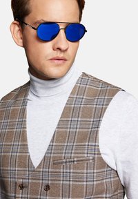 Okulary przeciwsłoneczne z niebieskimi lustrzanymi soczewkami i cienkimi czarnymi metalowymi oprawkami, noszone z szarym golfem i brązową kamizelką w kratkę z kieszenią.