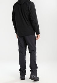 Veste imperméable noire avec capuche, associée à un pantalon cargo noir. Dotée de plusieurs poches, texture lisse et coutures renforcées.