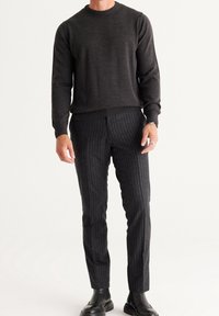 Dunkelgrauer gestrickter Pullover mit rundem Ausschnitt, kombiniert mit dunkel gestreiften Hosen. Die Hosen bestehen aus strukturiertem Stoff, im normalen Schnitt, und werden mit schwarzen Stiefeln getragen.