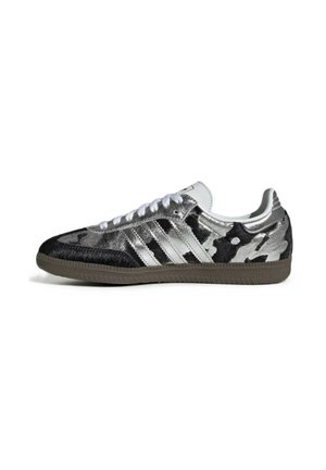 Low-top sneaker met zwart-zilver camouflagepatroon, witte veters, drie zilveren strepen aan de zijkant en een bruine rubberen zool.