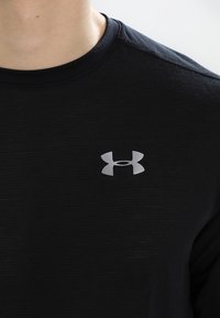 Black athletic shirt featuring a ribbed texture and a small silver logo on the chest. Short sleeves, round neck design.