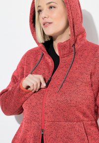 Veste à capuche zippée rouge avec un motif texturé, cordons de serrage réglables et zips de poche contrastants. Design à capuche avec poches latérales.