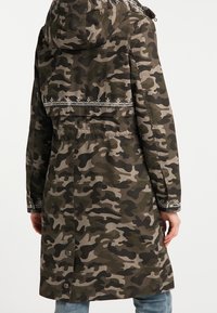 Parka de camuflaje en verde y gris. Presenta una capucha, detalles bordados y botones a presión. Confeccionada en una tela duradera con un diseño de longitud media.