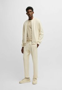 Set atletico color crema composto da una giacca bomber con zip, pantaloni con coulisse e sneakers coordinate, il tutto realizzato in morbido tessuto misto cotone.