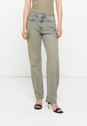 Jeans de mezclilla azul claro con corte recto, con bolsillos frontales y detalles embellidos, combinados con sandalias de tacón negras.