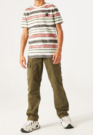 Niño de pie con una camiseta de manga corta a rayas, pantalones cargo verde oliva y zapatillas blancas con detalles negros.