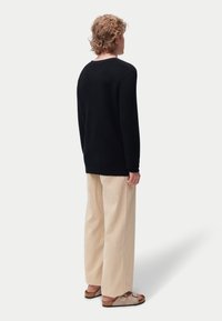 Pull côtelé noir à coupe décontractée, associé à un pantalon large crème et des sandales de couleur claire. Design minimaliste, sans logos visibles.