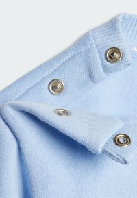 Vêtement col en tissu tricoté bleu clair avec des boutons-pression en argent et une texture douce, mettant en avant des lignes épurées et une finition soignée.