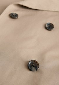 Material bej cu trei nasturi în patru găuri, colorați în nuanțe închise de marmură, aranjați într-un model triunghiular lejer.