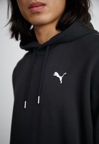 Sweat à capuche noir en mélange de coton, avec une poche kangourou à l'avant, arborant un logo Puma blanc sur la poitrine et des embouts argentés sur les cordons de serrage.