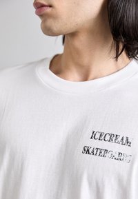 White cotton t-shirt with a crew neck, featuring black text "ICECREAM" and "SKATERGARDEN" in a slightly distressed font.