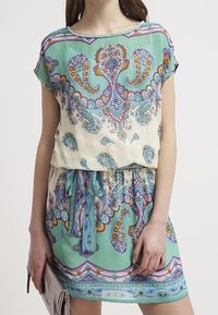 Lyhythihainen, paisley-kuvioinen mekko mintunvihreänä ja kermana. Mekossa on kapea vyötärö, johon kuuluu yhteensopiva vyö, ja kevyt, laskeutuva kangas.