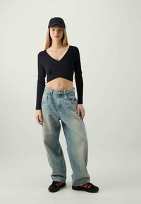 Schwarzer gerippter Crop-Top, lockere hellblaue Jeans mit ausgewaschenem Look, abgetragene Sneakers mit schwarzen und roten Akzenten sowie eine schwarze Mütze.