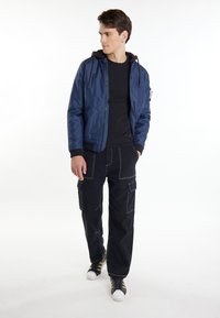 Giubbotto bomber navy con cappuccio nero, dotato di chiusura con zip, polsini a coste e due tasche laterali, abbinato a pantaloni cargo neri e sneakers.