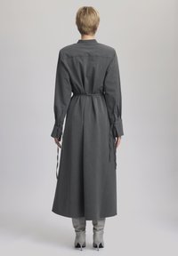Rochie lungă gri cu dungi fine, cu talie elastică, manșete cu nasturi și croi drept. Material moale cu o textură netedă.