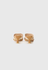 Tan open-back sandals with a block heel, featuring two crossing straps. Smooth texture with a minimalistic design and no visible embellishments.