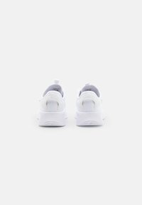 Białe sportowe sneakersy z teksturowaną podeszwą, miękką górą z materiału, pętlą na pięcie i minimalistycznym designem.