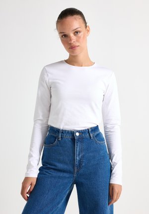 Hvid langærmet t-shirt med rund hals, parret med højtsiddende blå denim wide-leg jeans med forlommer og knaplukning.