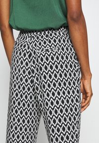 Pantalon noir et blanc à motif avec une poche arrière étroite, fabriqué en tissu doux. Le design présente un motif losange allongé.