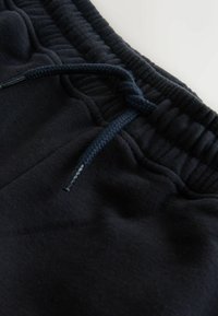 Pantaloni de trening bleumarin, cu talie elastică și șnur. Material moale, cu textură netedă și ușor lucios.
