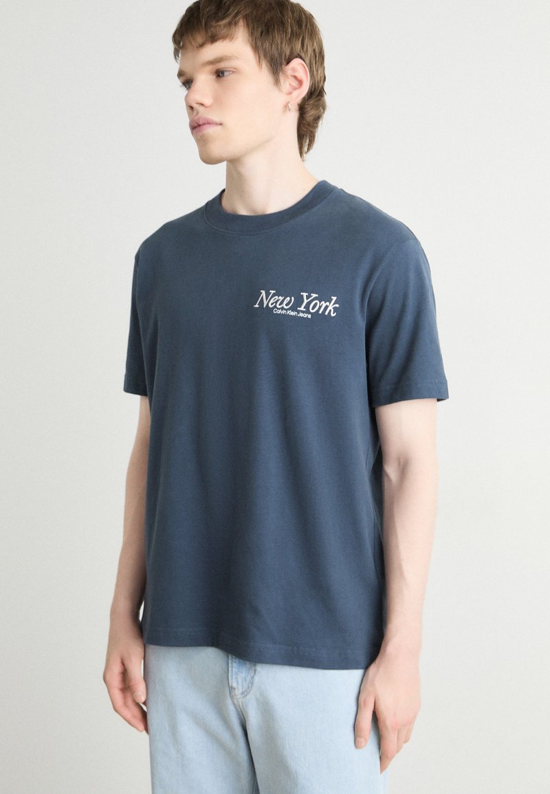 Marineblauwe katoenen t-shirt met korte mouwen, ronde halslijn en "New York" in het wit geborduurd op de linkerkant van de borst. Gladde textuur.