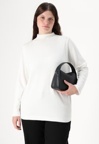 White long-sleeve top with a high neck, paired with a small black leather handbag featuring a structured, curved design.