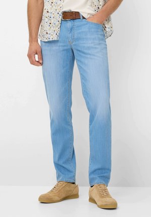 Lichtblauwe denim jeans met een rechte snit, voorzien van subtiele vervaging, vijf zakken en een bruine riem. Gecombineerd met beige sneakers.