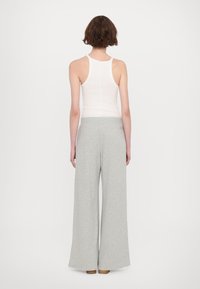 Grijze wijde broek gemaakt van een zachte, gladde stof, gecombineerd met een aansluitend wit tanktop. De outfit heeft een ontspannen stijl en een eenvoudig ontwerp.
