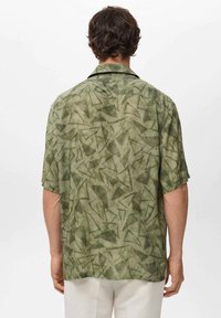 Camisa de manga corta en verde claro, con un patrón texturizado de formas abstractas, terminada con un cuello clásico y un ajuste relajado.