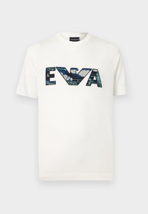 White short-sleeve T-shirt with large blue-green sequin letters "EVA" and a stylized eagle logo in the center.