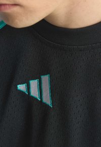 Czarna koszulka sportowa z teksturowanym wzorem, okrągłym dekoltem oraz logo w kolorze turkusu i srebra z trójkątnymi akcentami na froncie.