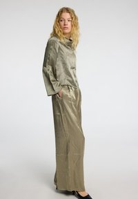 Olive green, shiny fabric two-piece outfit featuring a loose-fit top with long sleeves and wide-leg pants with side pockets and a smooth texture.