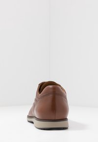 Chaussure en cuir marron à texture lisse, talon arrondi et semelle contrastante ; présente des coutures discrètes et des éléments de design minimalistes.