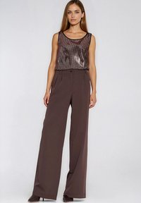 Brązowe spodnie o szerokich nogawkach w połączeniu z bezrękawnym, błyszczącym, brązowym topem z zaokrąglonym dekoltem i fakturowaną powierzchnią.