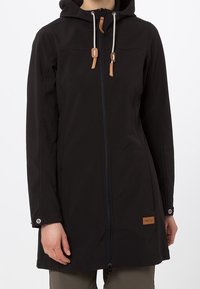 Abrigo negro impermeable con capucha, que cuenta con un cierre completo, acentos de cuero en los cordones y un parche de logo en la parte inferior delantera.