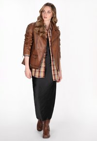 Brun læder bikerjakke over en ternet skjorte, parret med en sort satin maxi-nederdel og brune ankelsko med metalaccenter.