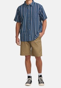 Short-sleeve button-up shirt with blue and white vertical stripes, paired with khaki shorts. Black high-top sneakers and white socks visible.
