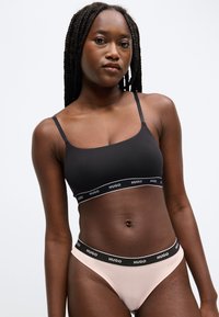 Zwarte bralette met dunne bandjes en logo-elastiek, gecombineerd met lichtroze string met bijpassende logoband. Gladde stoftextuur.