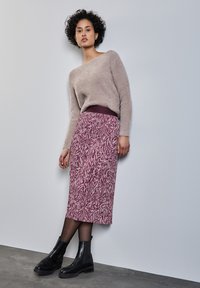 Maglione beige chiaro fuzzy con vestibilità over, abbinato a una gonna a tinta unita color malva lunga fino al ginocchio e stivaletti neri alla caviglia.