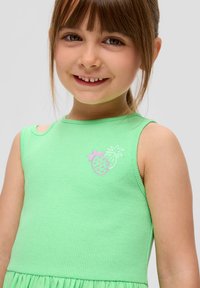 Grün gestreiftes Kleid mit rundem Ausschnitt und ärmellosem Design. Auffällige pinke Ananas-Stickerei auf der Brust. Strukturierter Stoff.
