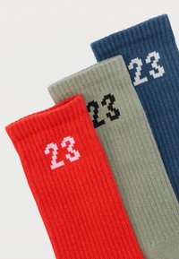 Τρία ζευγάρια ριγωτές κάλτσες σε κόκκινο, λαδί και μπλε, κάθε ένα με τον αριθμό «23» πλεκτό σε λευκό ή μαύρο στο μανσίλι.