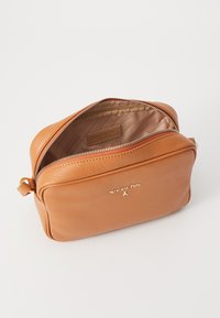 Borsa in pelle color tan con chiusura a zip, interno foderato e logo dorato. Presenta una forma rettangolare e una superficie testurizzata.