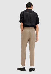 Camicetta in satin nera a maniche corte abbinata a pantaloni beige, con tasche laterali e risvolti, completata da scarpe nere e calze bianche.