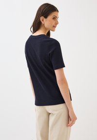 Košile s krátkým rukávem v námořnické modři z texturované látky s kulatým výstřihem a ležérním střihem, doplněná světle béžovými kalhotami.