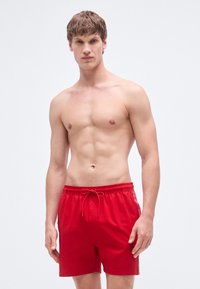 Κόκκινα μαγιό σορτς με κορδόνι στη μέση, με λογότυπο στο πλάι, άνετη εφαρμογή και ελαφρύ ύφασμα. Δεν φοριέται επιπλέον ρούχο.