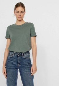 Kurzärmliges, Rundhals-T-Shirt aus olivgrüner Baumwolle, kombiniert mit hochgeschnittenen blauen Denim-Jeans, die Vordertaschen und eine lockere Passform bieten.