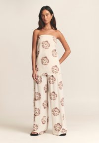 Be rankovių palaidinė ir plačios kelnės iš lengvos kreminės spalvos audinio su gėlių raštu ramių rudų atspalvių. Lygus tekstūra, laisvas kirpimas.