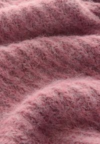 Tissu tricoté rose doux et duveteux avec un motif texturé légèrement bouclé et des fibres visibles créant une apparence chaleureuse.